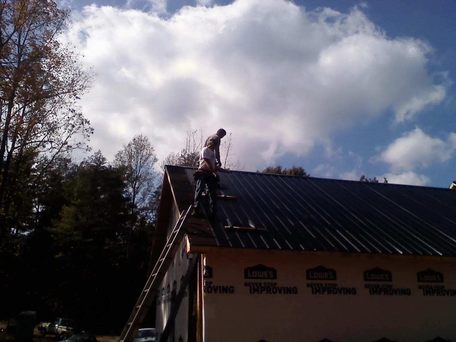 Roofer fastening dark metal panels high against a cloudy sky, from a Roof Inspection job in Somers